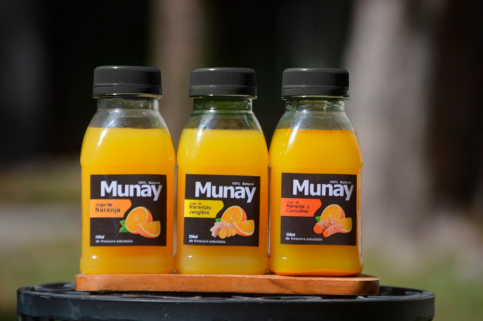 Tres botellas de zumo MUNAY de naranja y jengibre, naranja y curcuma, y naranja.
